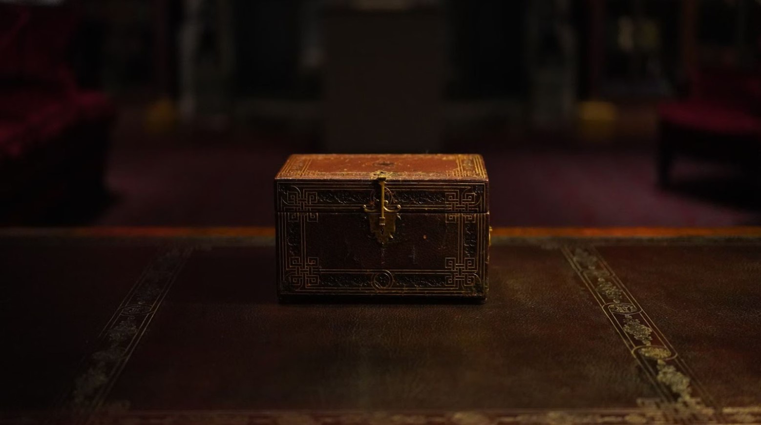 A treasure box that is closed and placed on a wooden table. The box is made of wood with gold detailing and the table has a similar pattern.