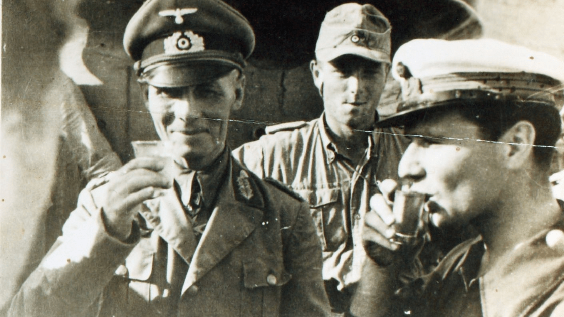 Black-and-white photo of Erwin Rommel holding a small glass and grinning. He is standing beside some troops.