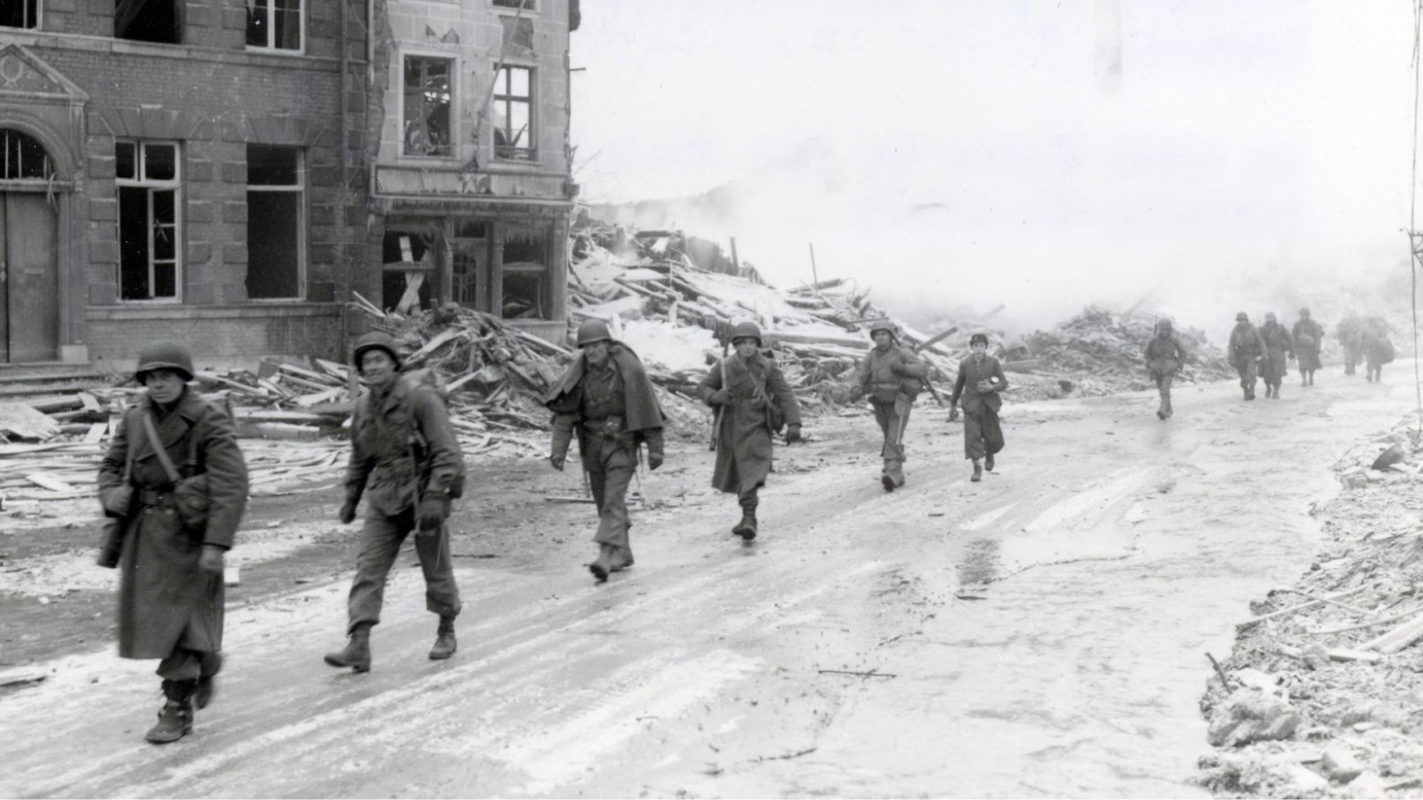 A line of U.S. soldiers walking into a bombed European city during World War II.