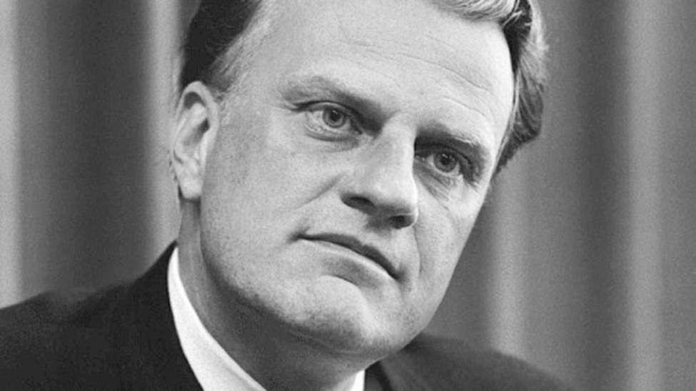 A black and white photo of Billy Graham. He has his head slightly tilted and appears to be listening intently.