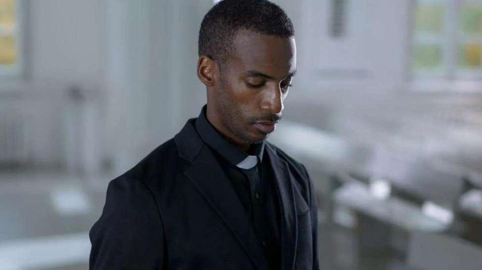 A pastor wearing all black with a white collar.