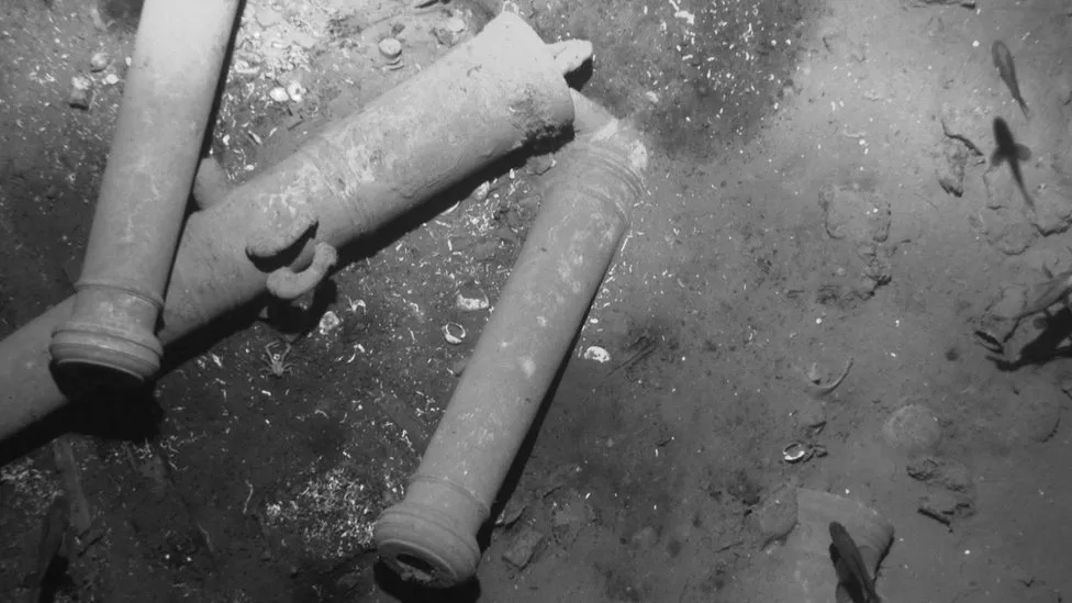 A grey scale underwater image of ship canons on the sea floor