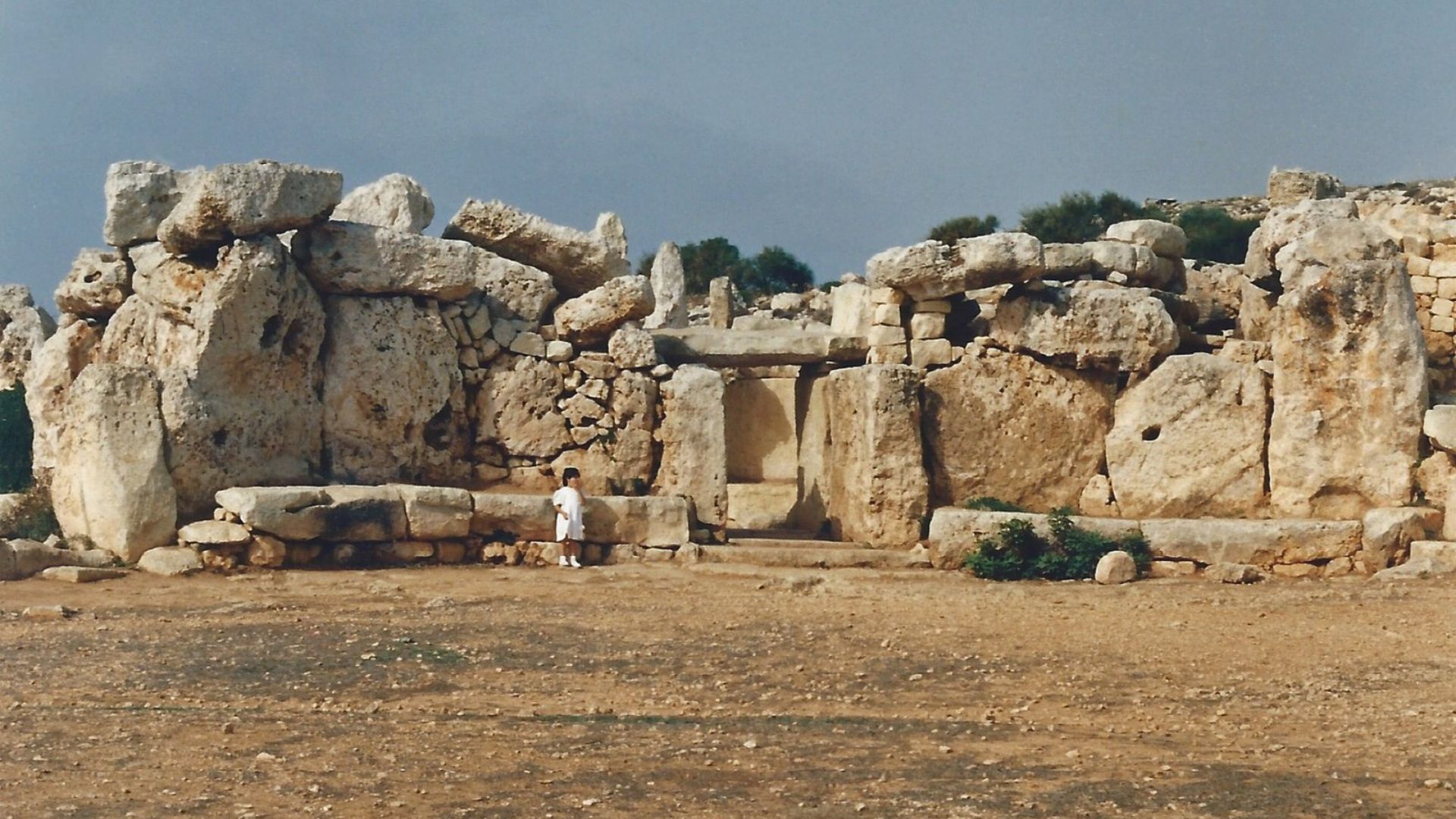 A person in white clothing stands to the left side of an ancient megalithic temple complex
