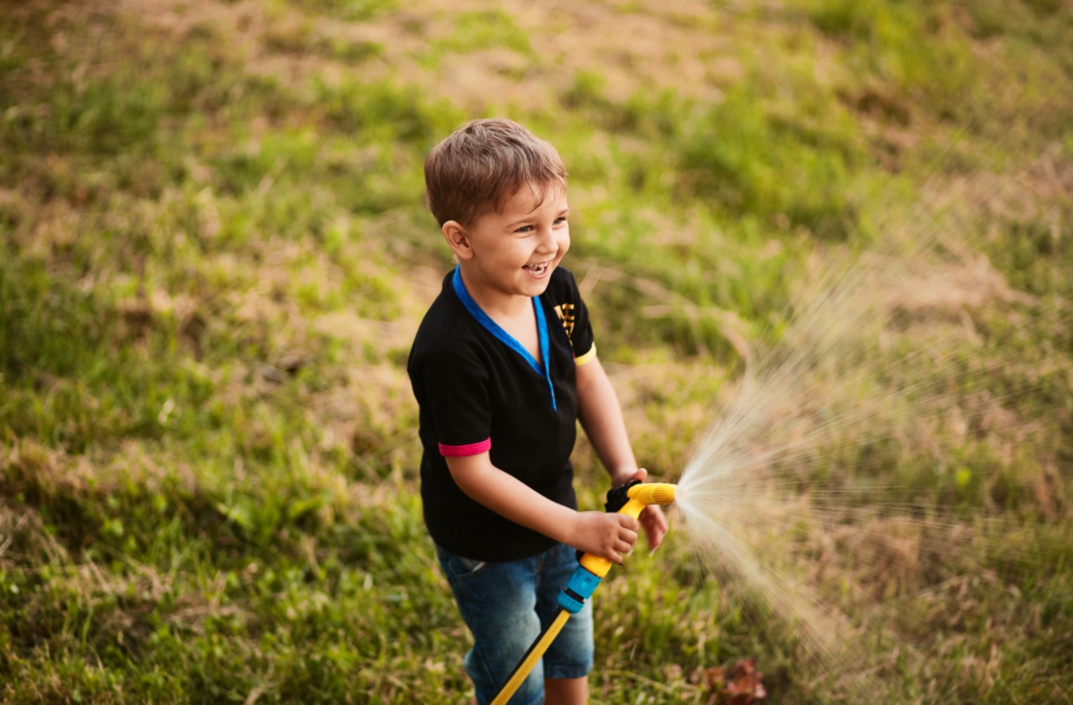 A young child is pictured playing with a garden hose in his backyard