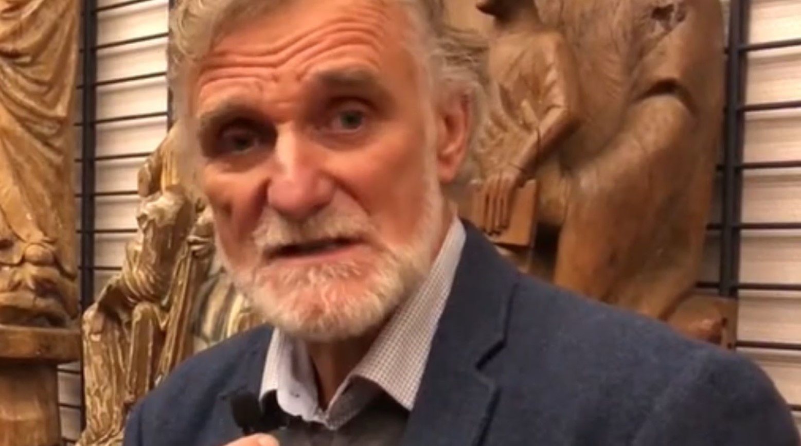Jon Anders Risvaag. He is holding a mic and is talking to the camera. There are some gold statues behind him against a wall.