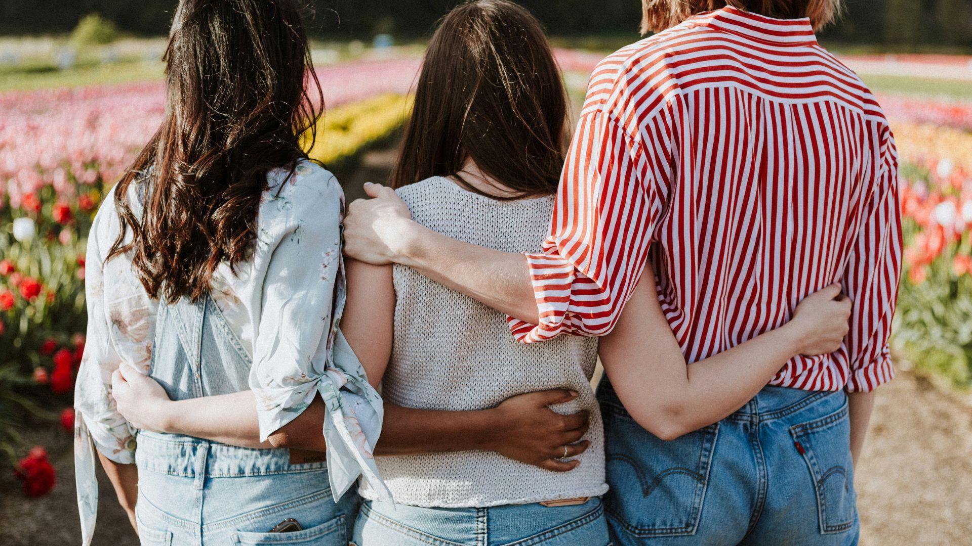 Three girls walking with their arms around each other’s backs.