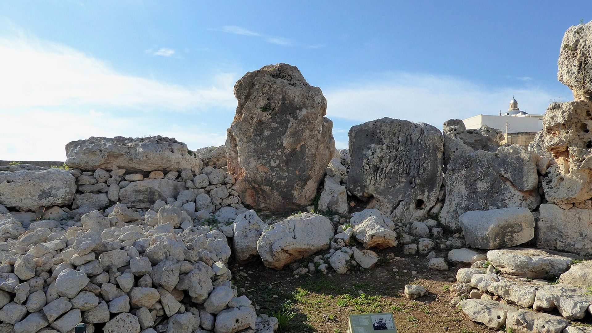 Image of ancient megalithic ruins in Malta under a clear blue sky. Large limestone boulders, some weathered and covered with lichen, form the remains of a prehistoric structure