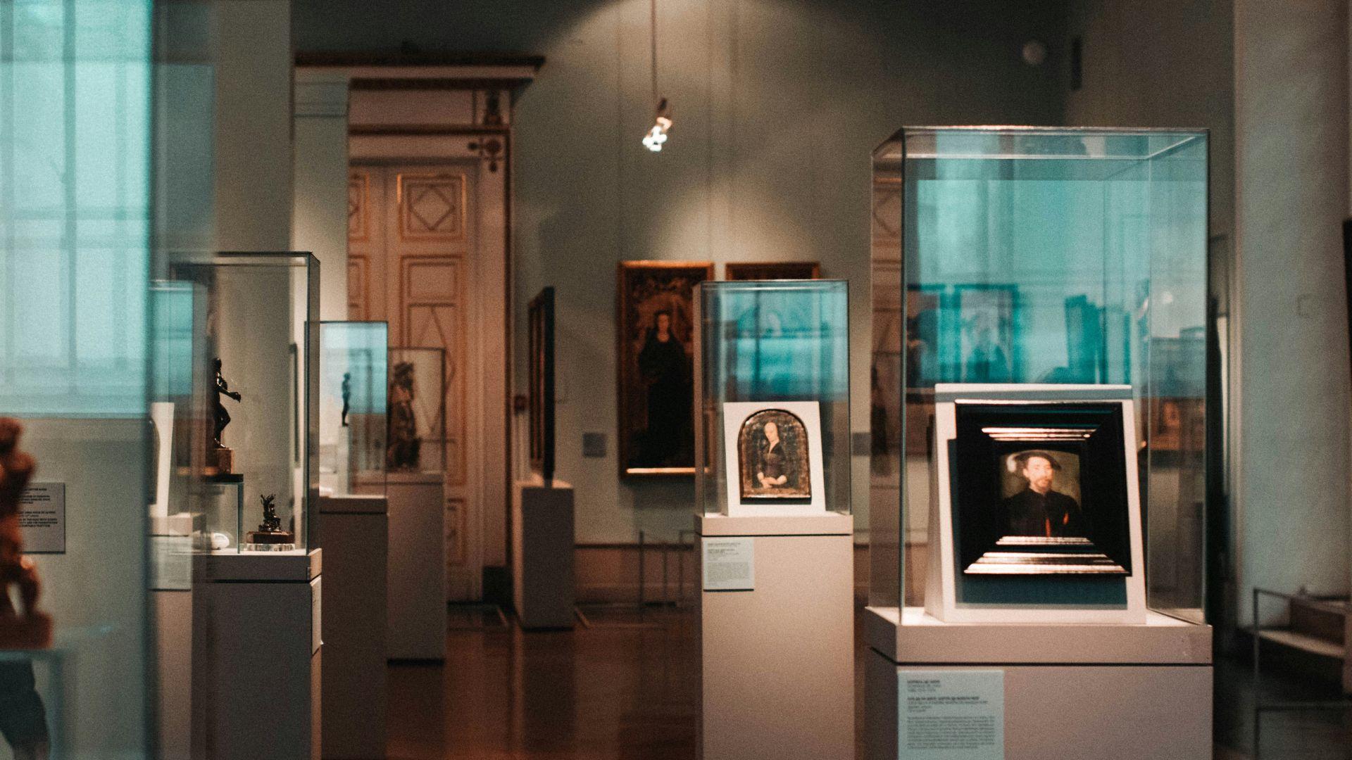A museum with paintings and art on pillars around the room, behind glass walls.