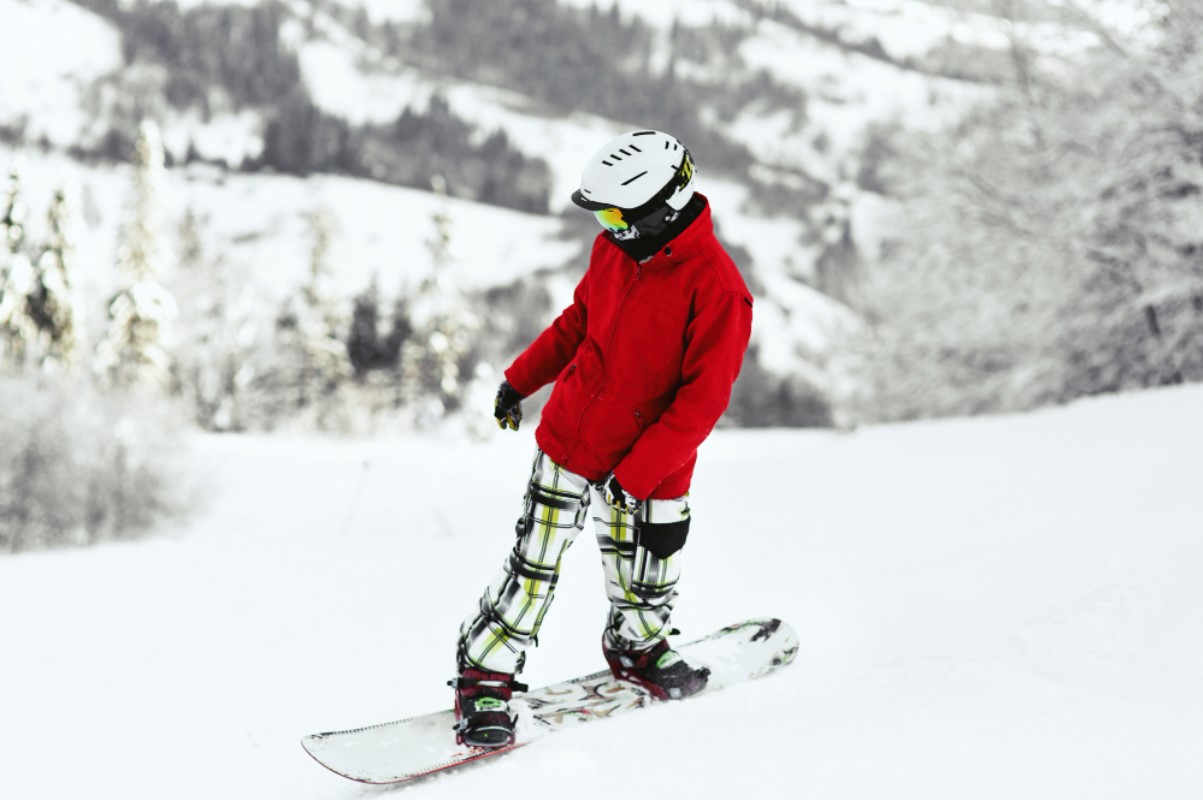 A person dressed in a large red coat is pictured snowboarding down a mountain