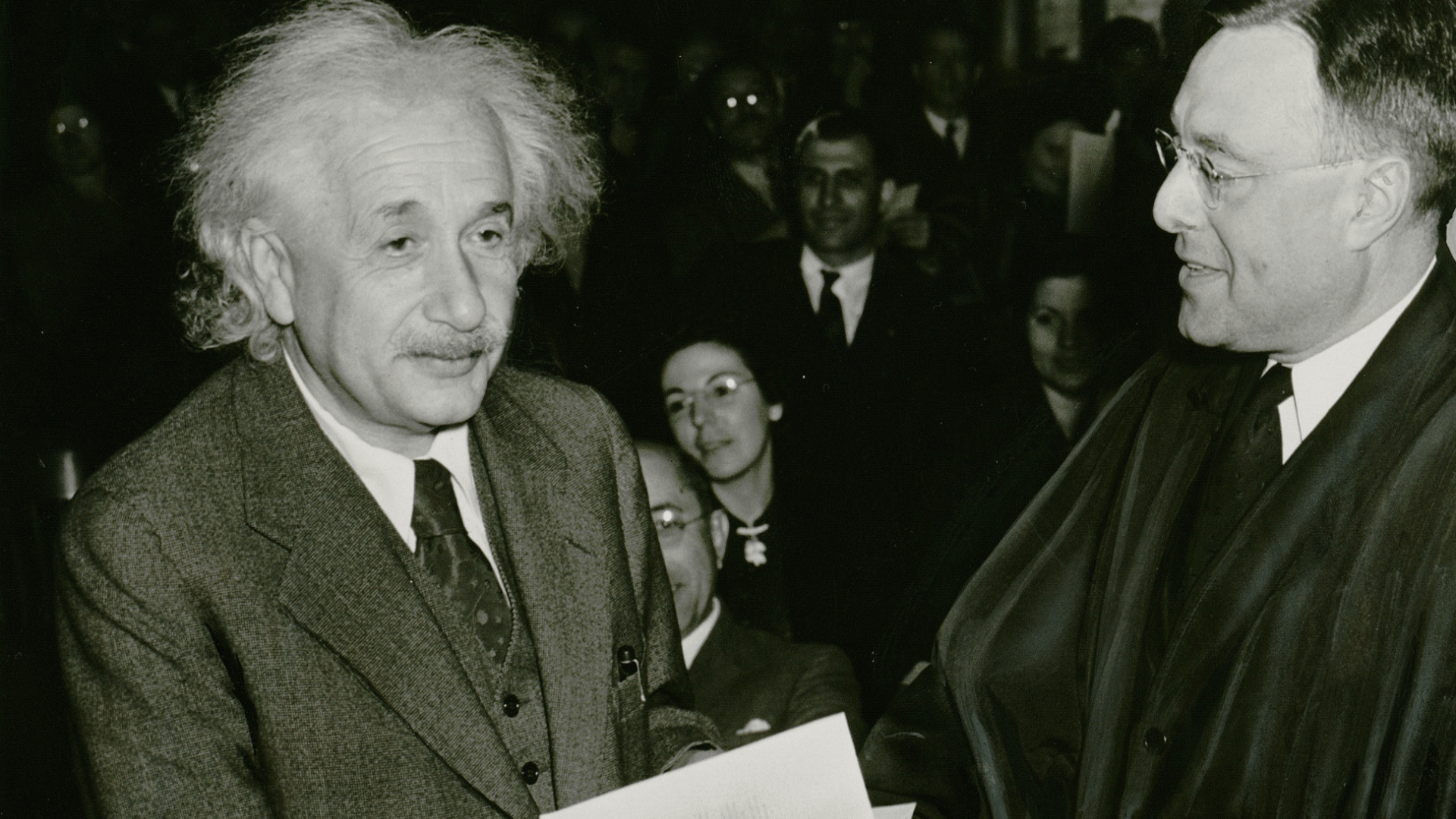 Black-and-white photo of Albert Einstein in a suit as an old man receiving an honorary degree.