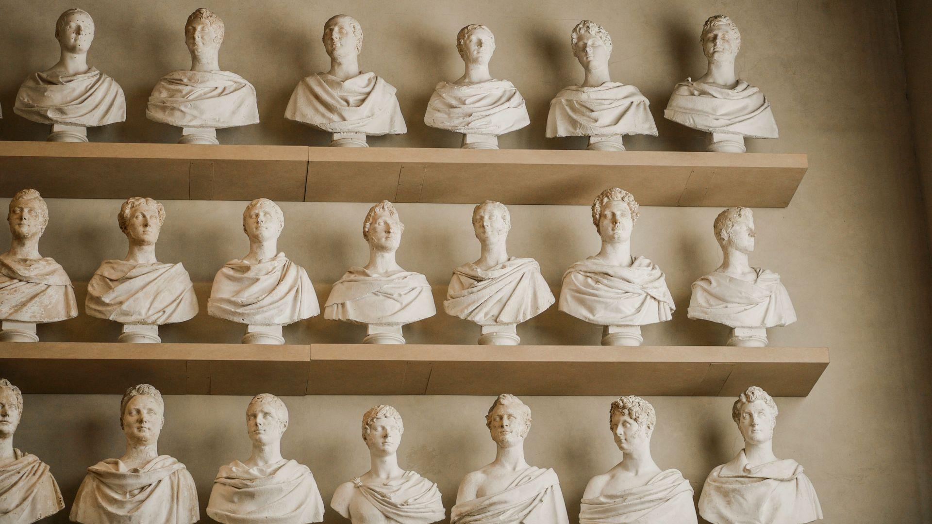 Three shelves full of many white statues of old Italian figures.