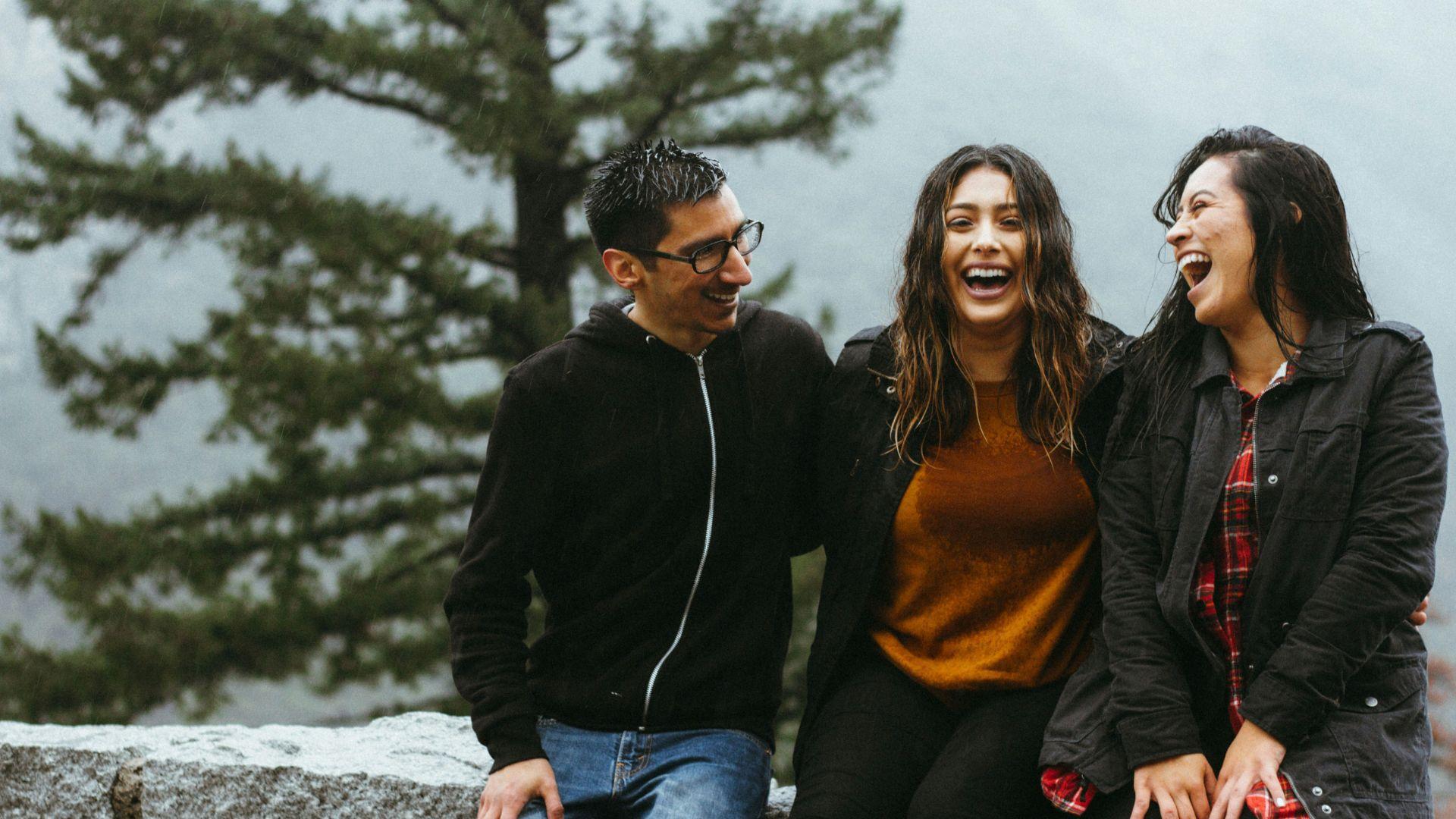 A man and two women sitting and smiling together while in a rain storm.