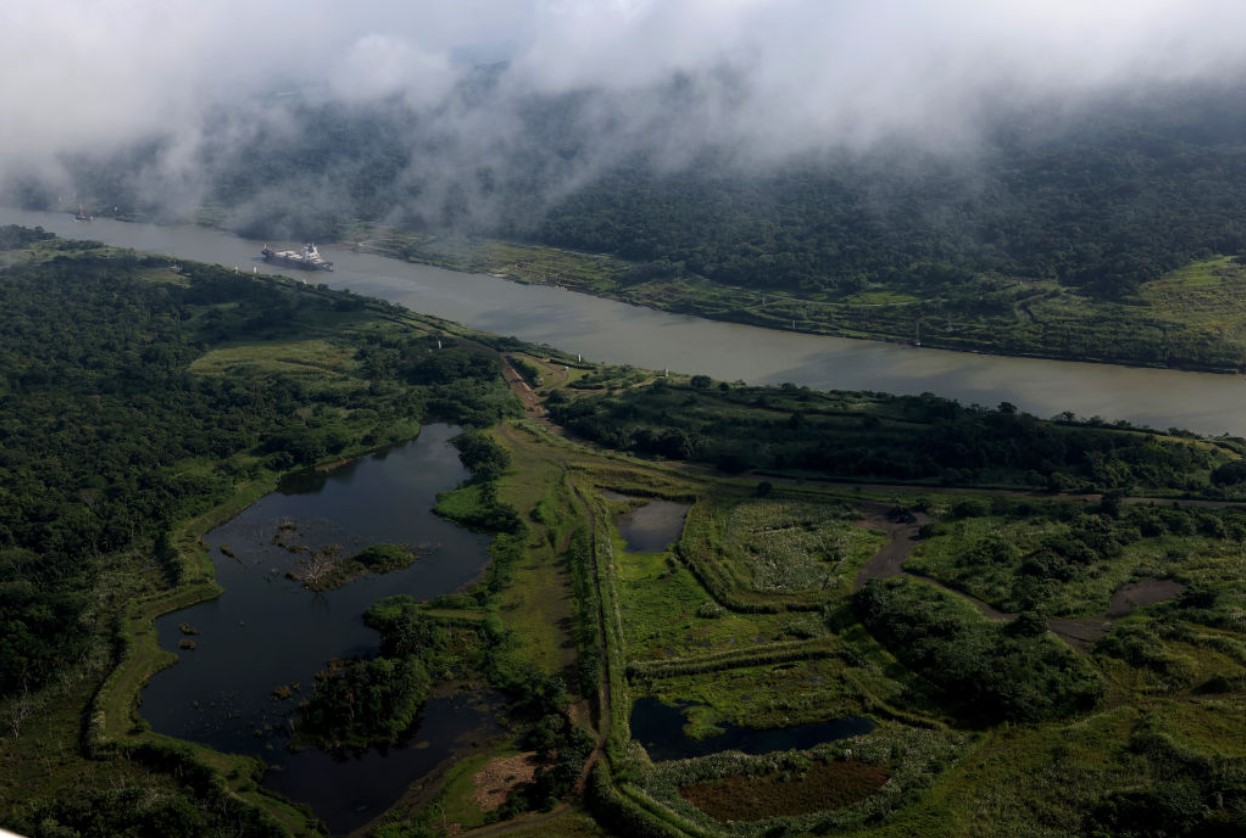 In an aerial view, a tugboat assists a ship as it navigates the Chagres River while it transits through the Panama Canal