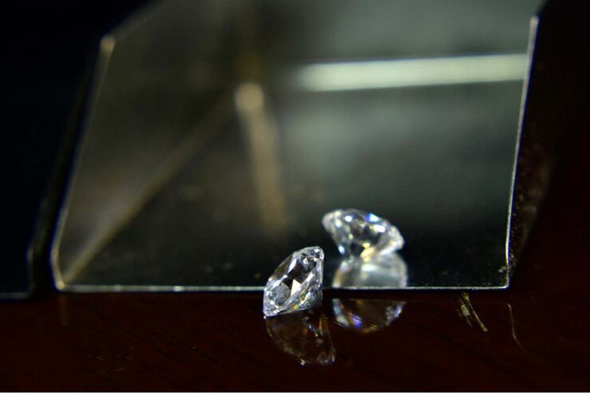 An image of a large diamond as it rests on a wooden table beside a mirror