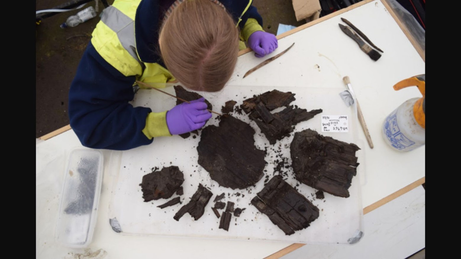 Cleaning a fragile wooden bucket base from the burnt debris beneath a structure