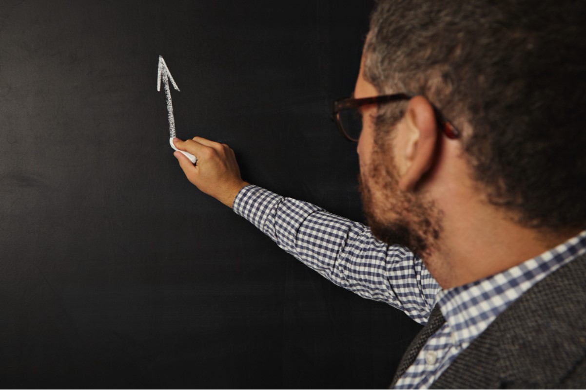 A college professor is pictured writing on a blackboard