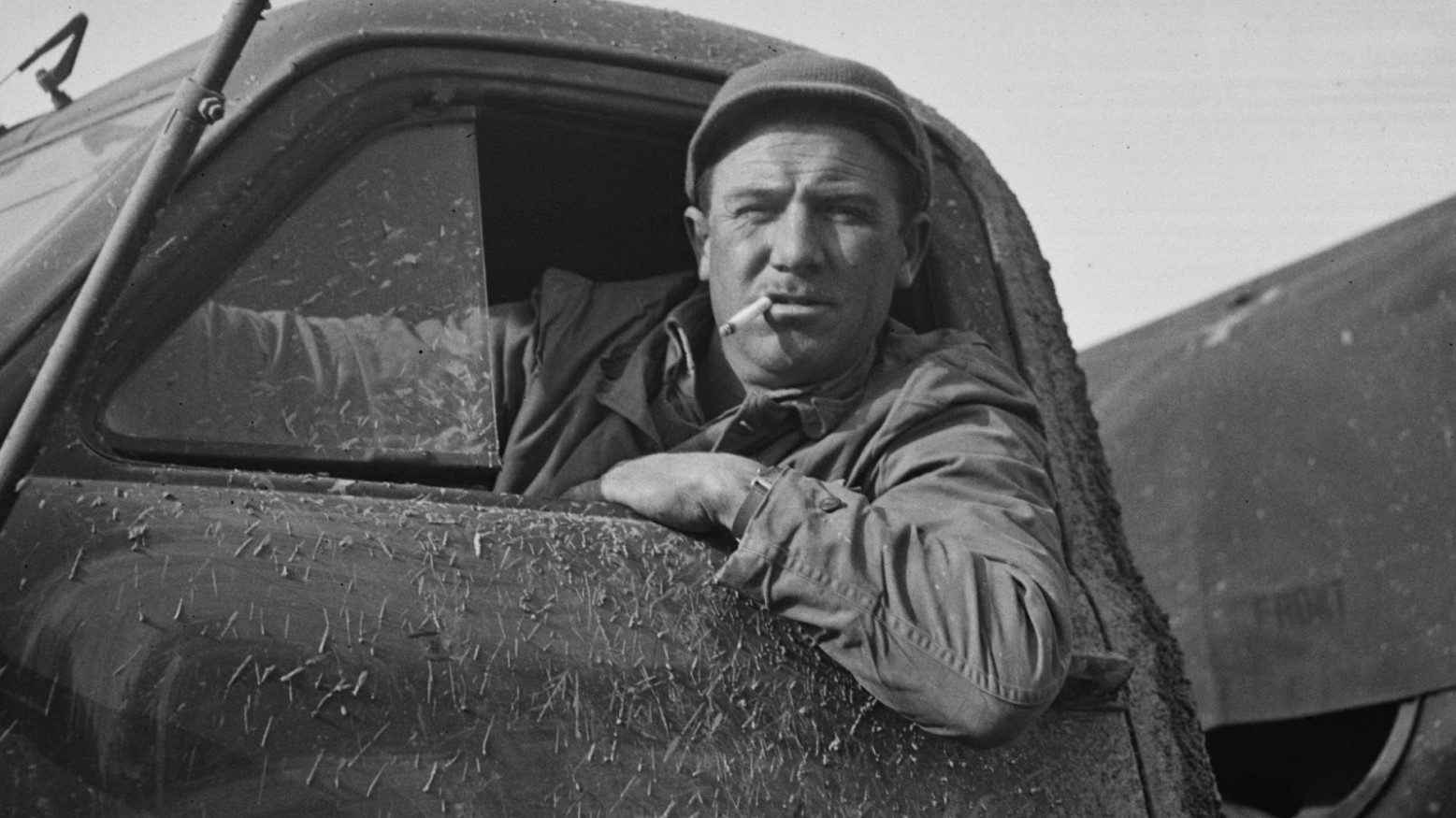 A black and white photo of a U.S. soldier driving a truck during World War II.