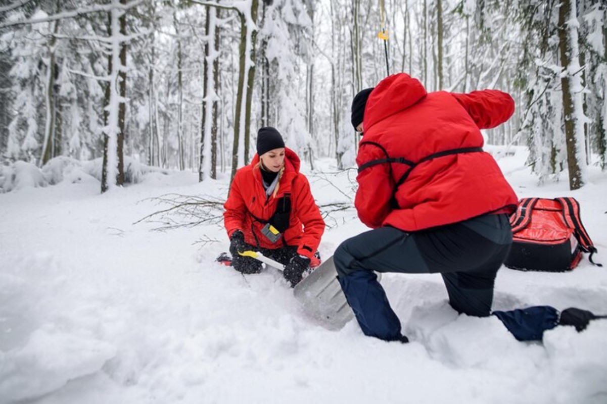 Two members of a search and rescue party are pictured digging into the snow