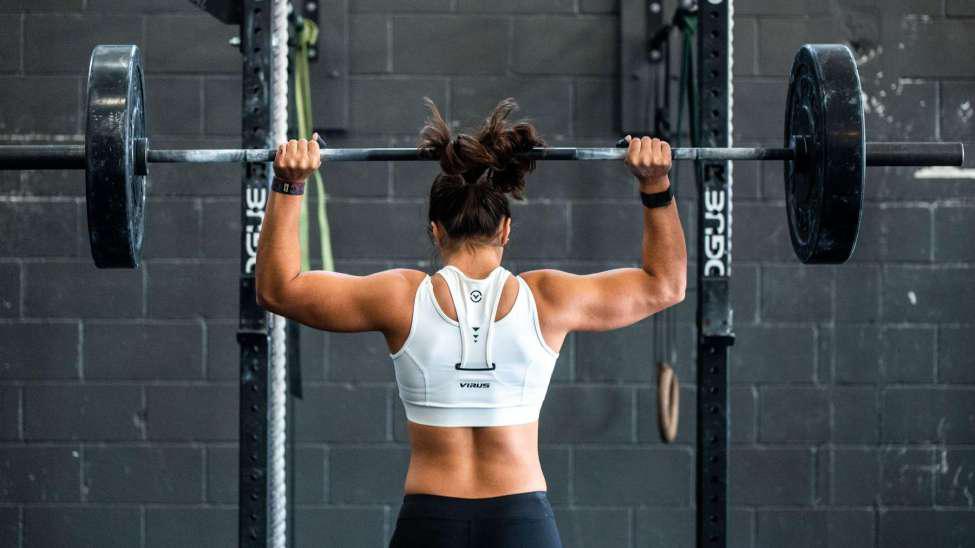 A woman wearing a sports bra and leggings and is lifting a heavy weight.