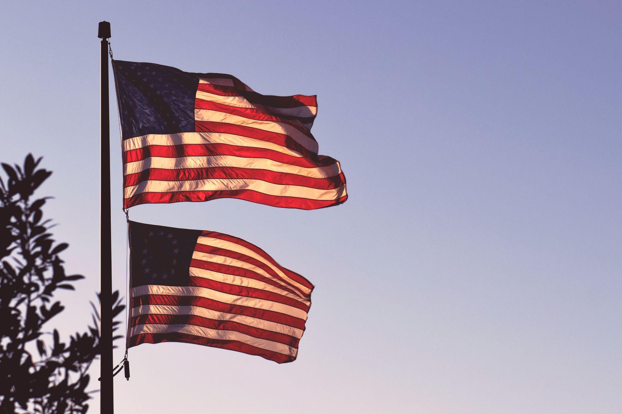 Two American flags on a pole in the daytime.