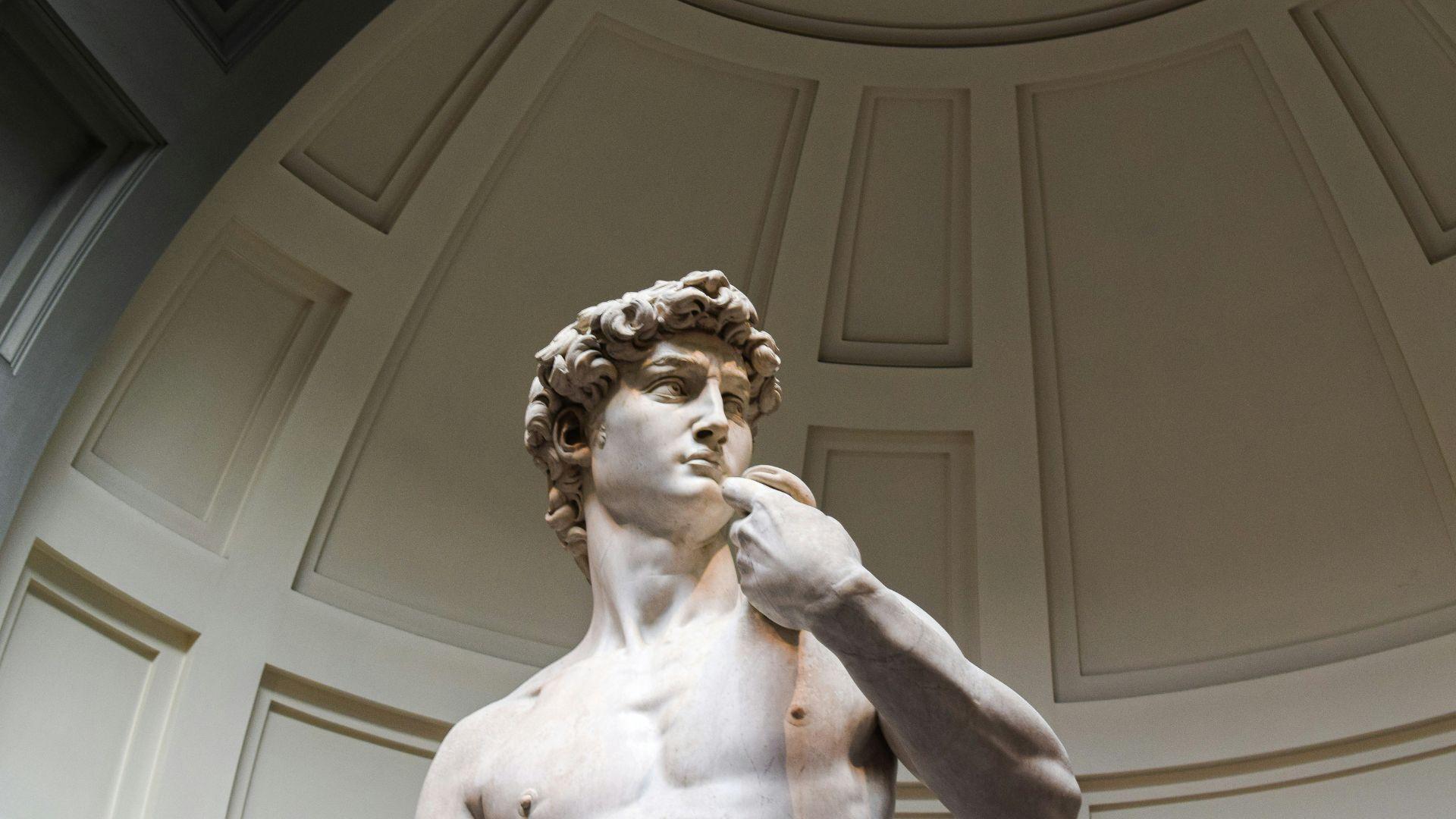 Michelangelo’s David statue seen underneath a dome in a museum.