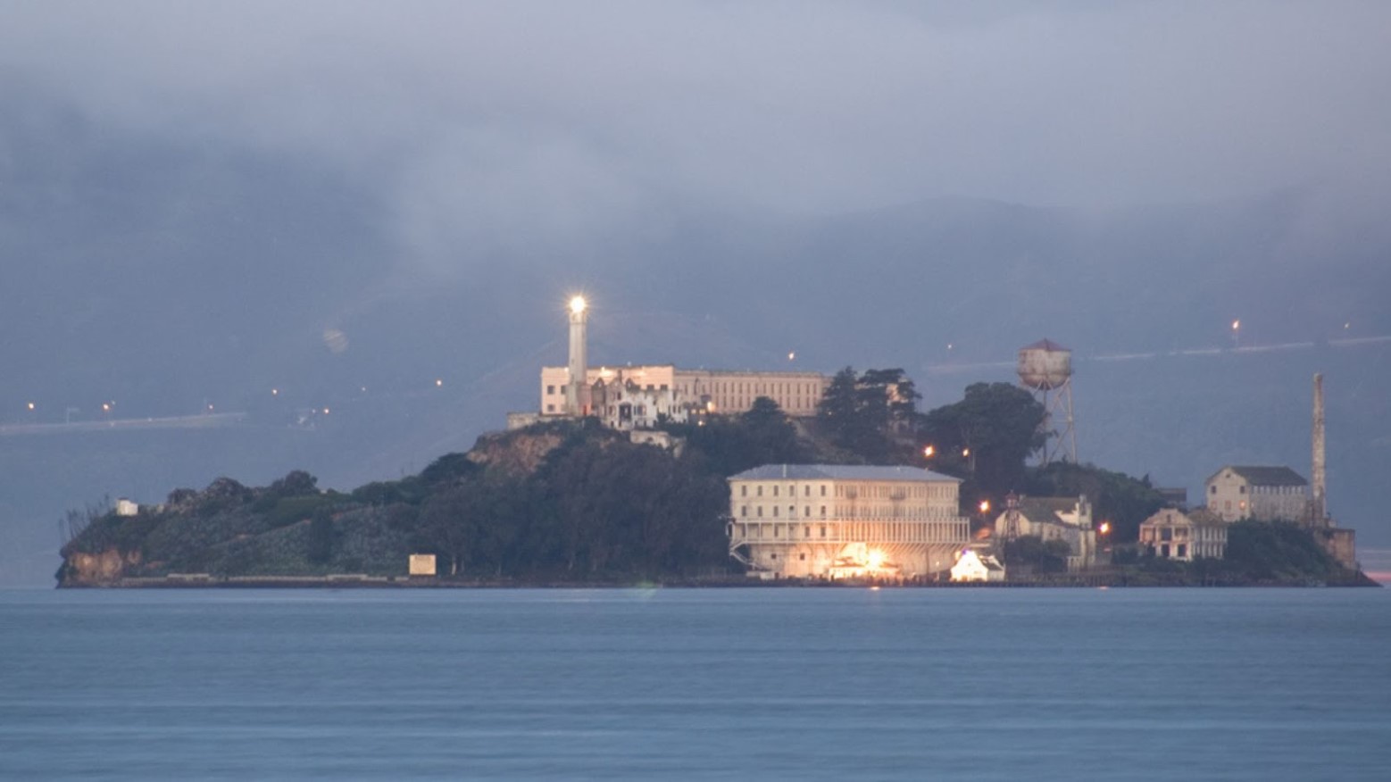 Alcatraz Island at night. The island is lit up and there is fog surrounding it, which makes it difficult to see anything in the distance.