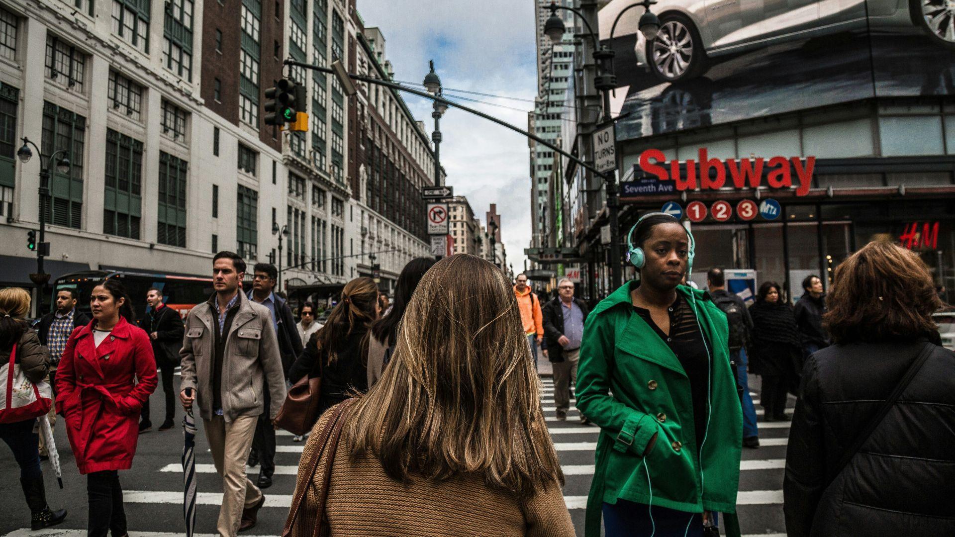 Many people walking on a crosswalk in the daytime in New York City.