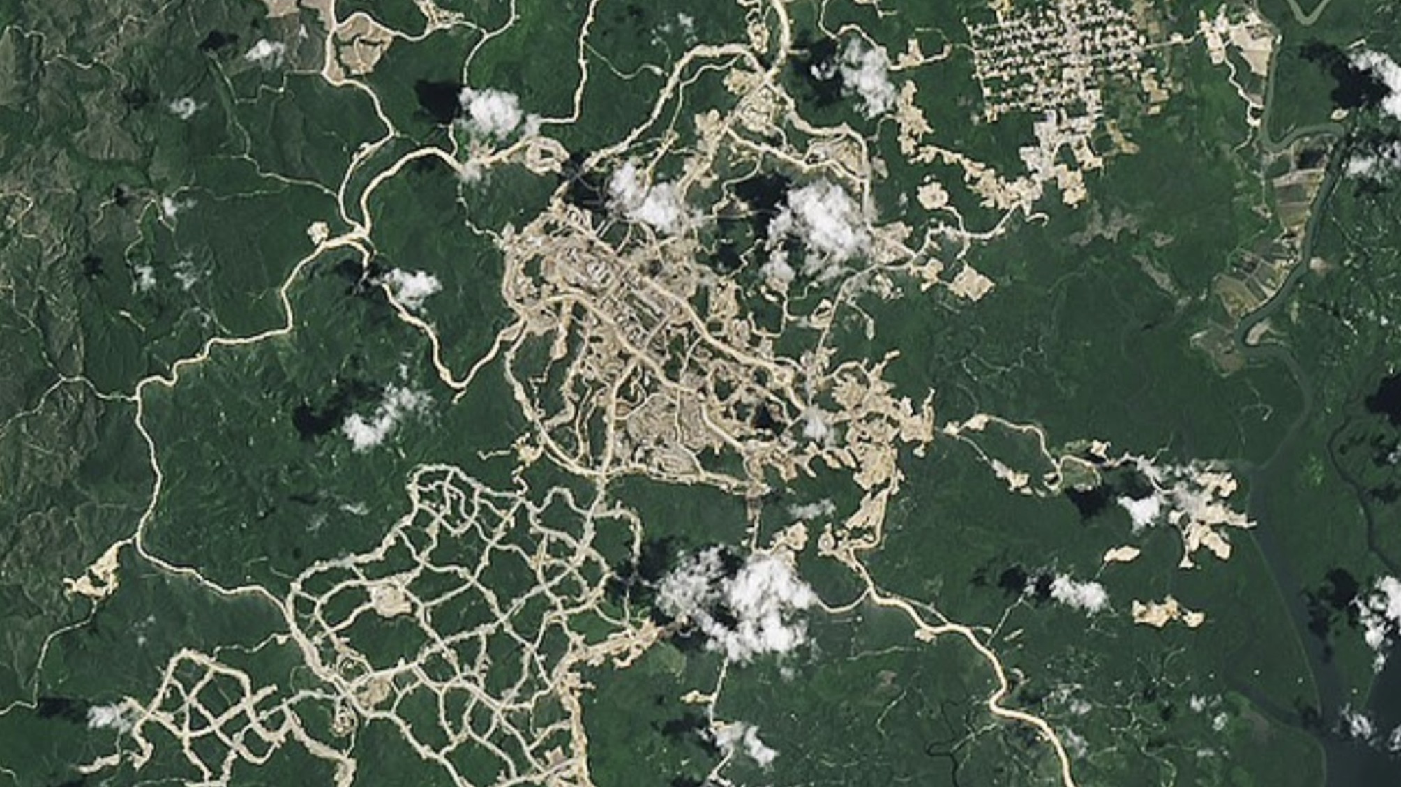An aerial view of Nusantara. There are green fields and roads, and clouds are above the city.