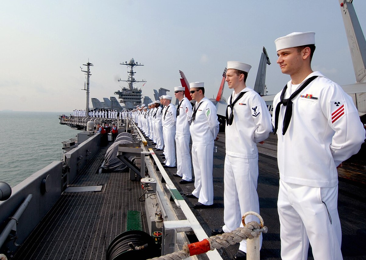 An image of several US Navy sailors lined up and looking out to sea