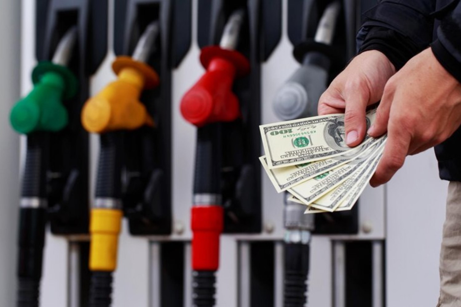 An image of a man holding several $100 bills beside a gas station
