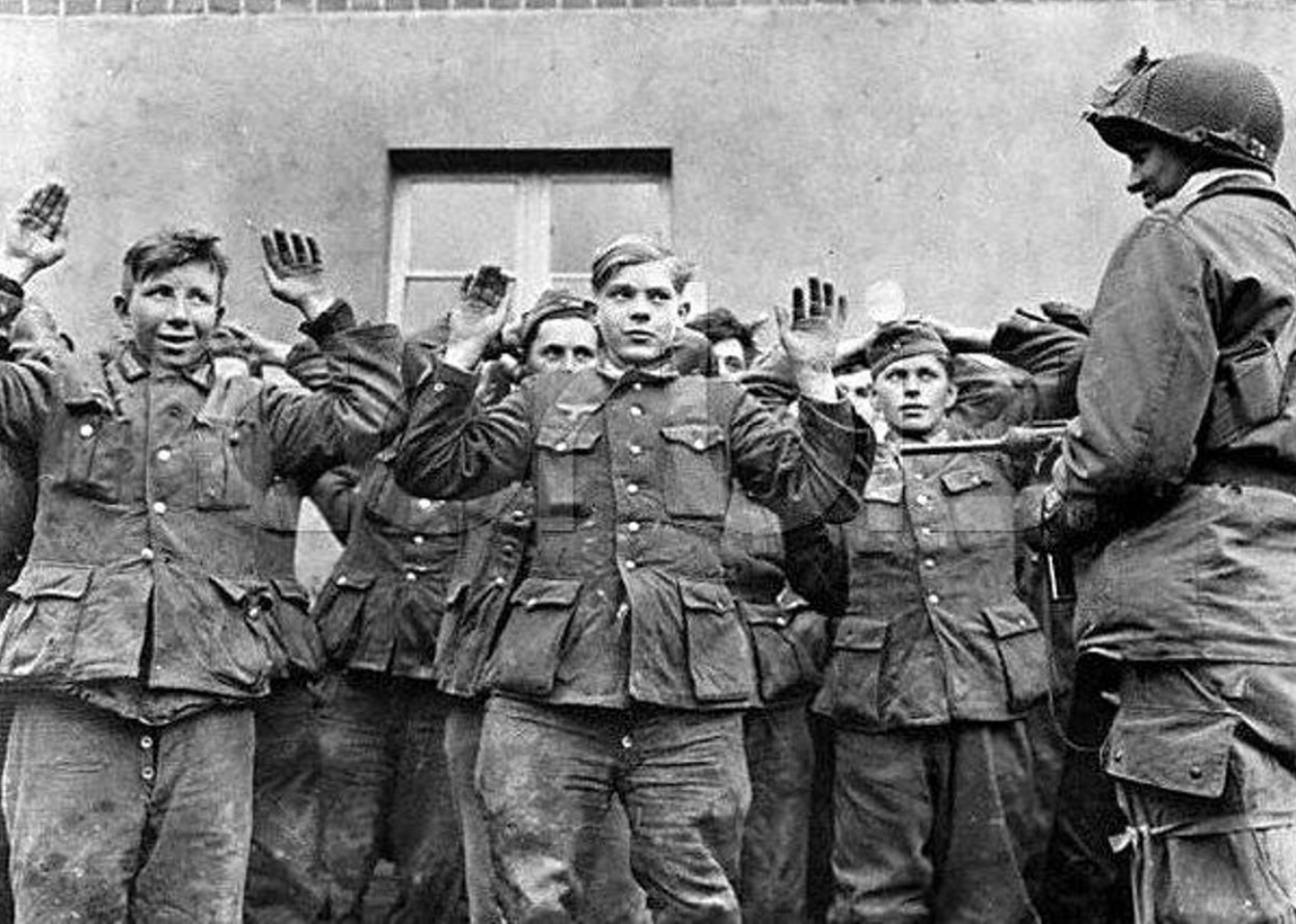 Several prisoners during WWII hold their hands up in front of a guard