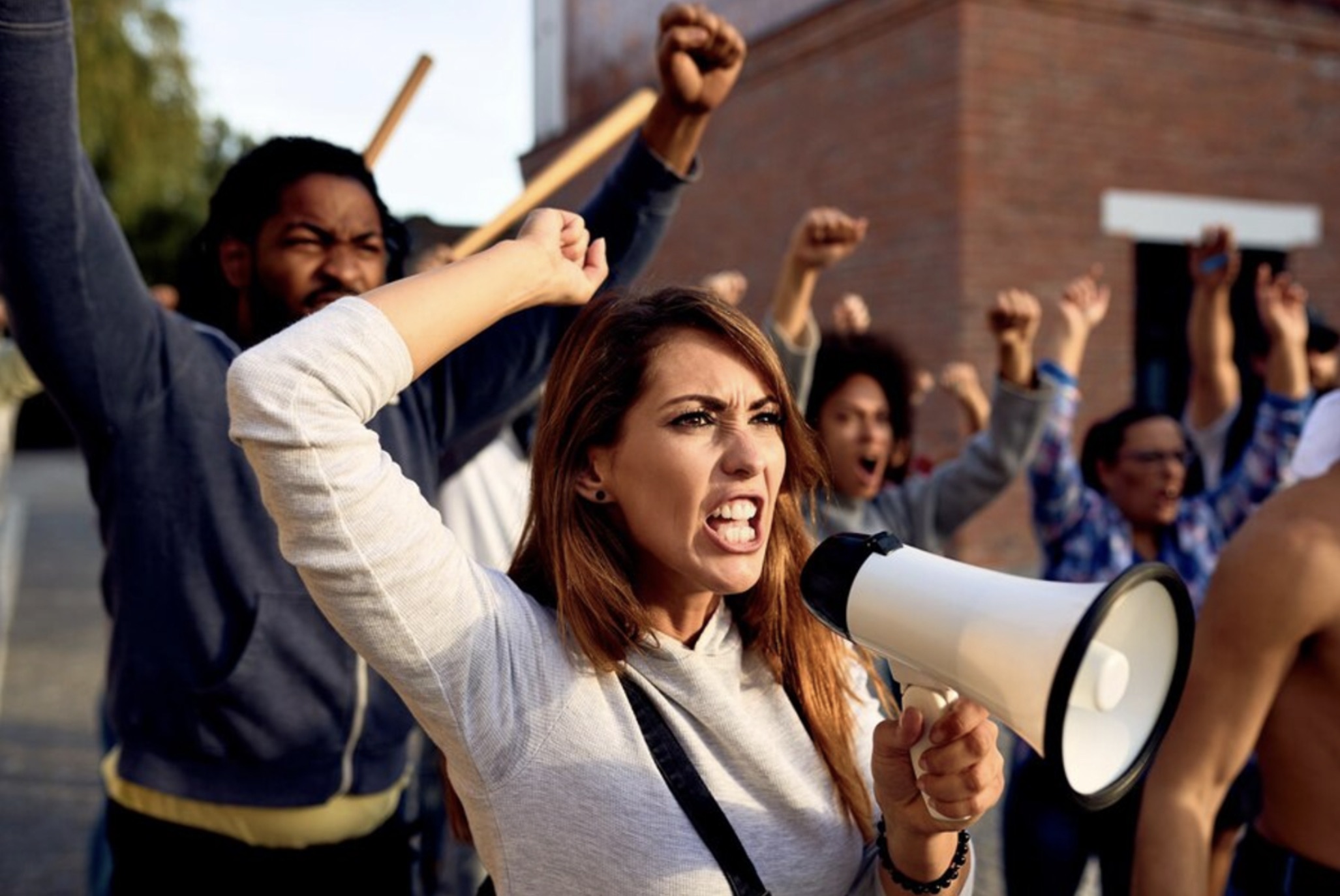 Several people yelling at a protest behind one woman with a megaphone