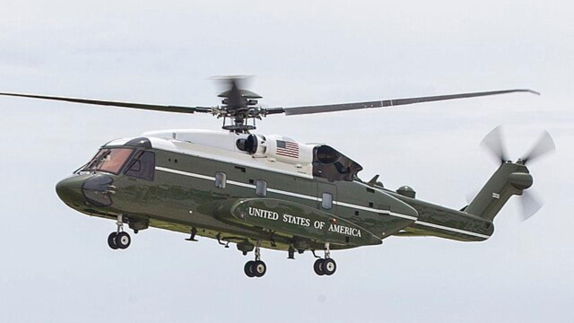 The VH-92 helicopter. It is green and white and has an image of the American flag on it. At the bottom of the helicopter, it says “United States of America” in white.
