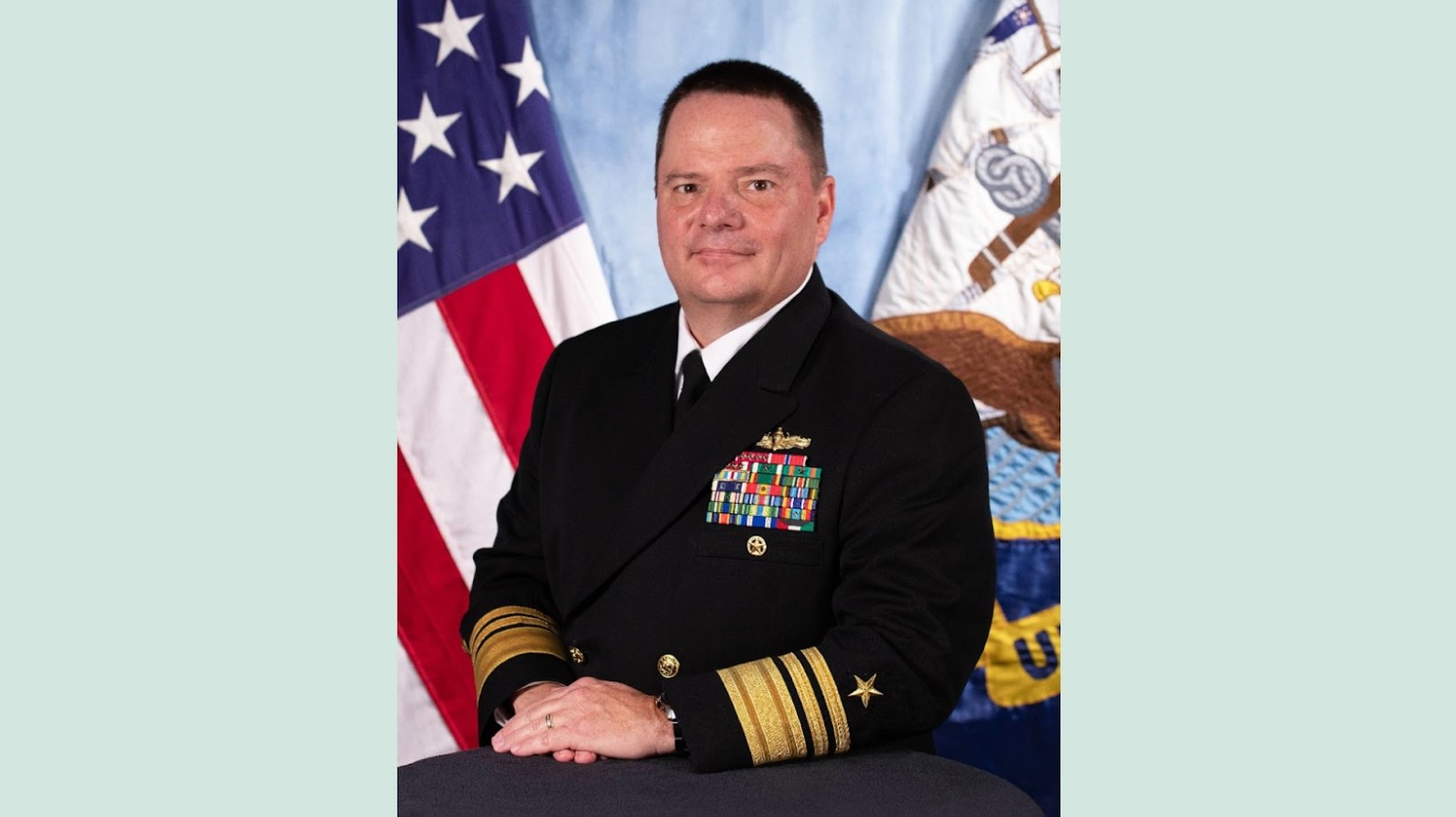 A man wearing the Navy Vice Admiral uniform posing in front of a couple of flags