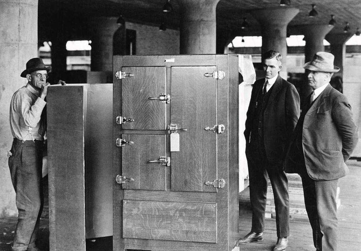 Several men standing alongside one of the first refrigerators