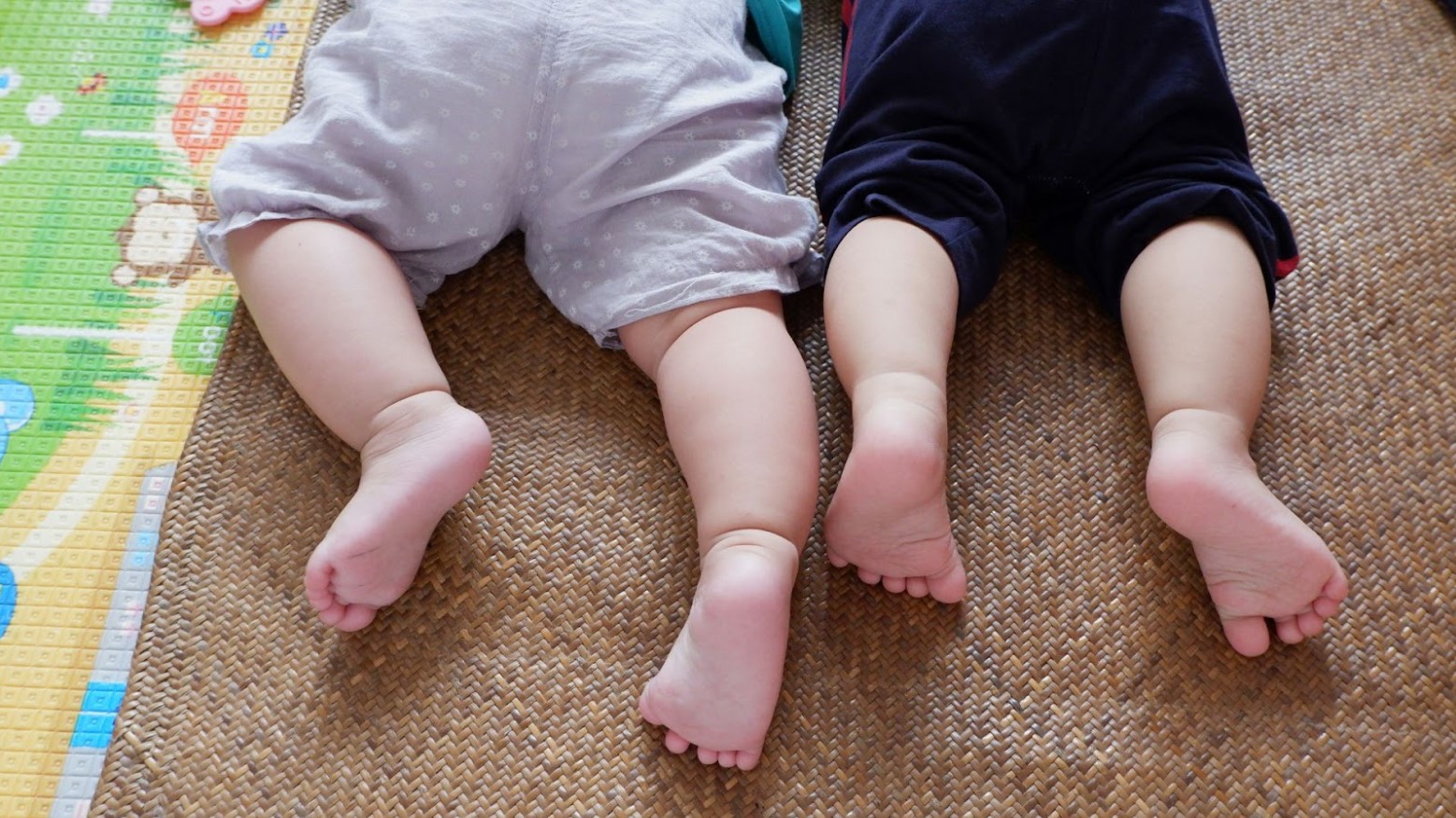 Two babies laying down on the ground and crawling.