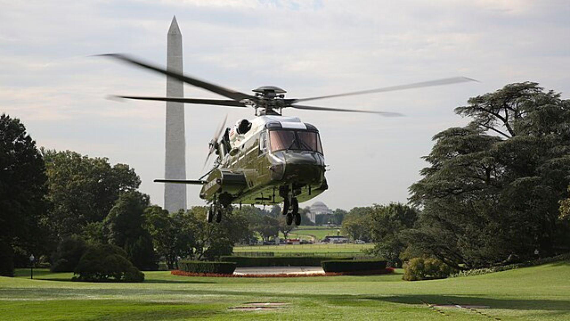 The VH-92 helicopter is preparing to land on the lawn at the White House. The Washington Monument is in the background.
