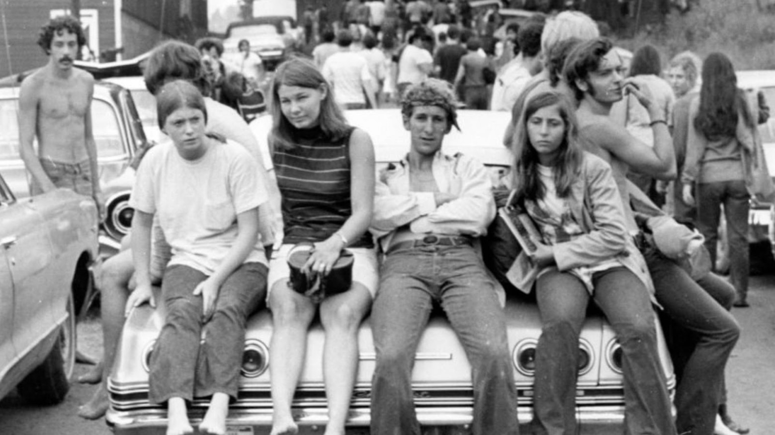 An old black and white photo of people sitting on the back of a car at Woodstock in 1969.