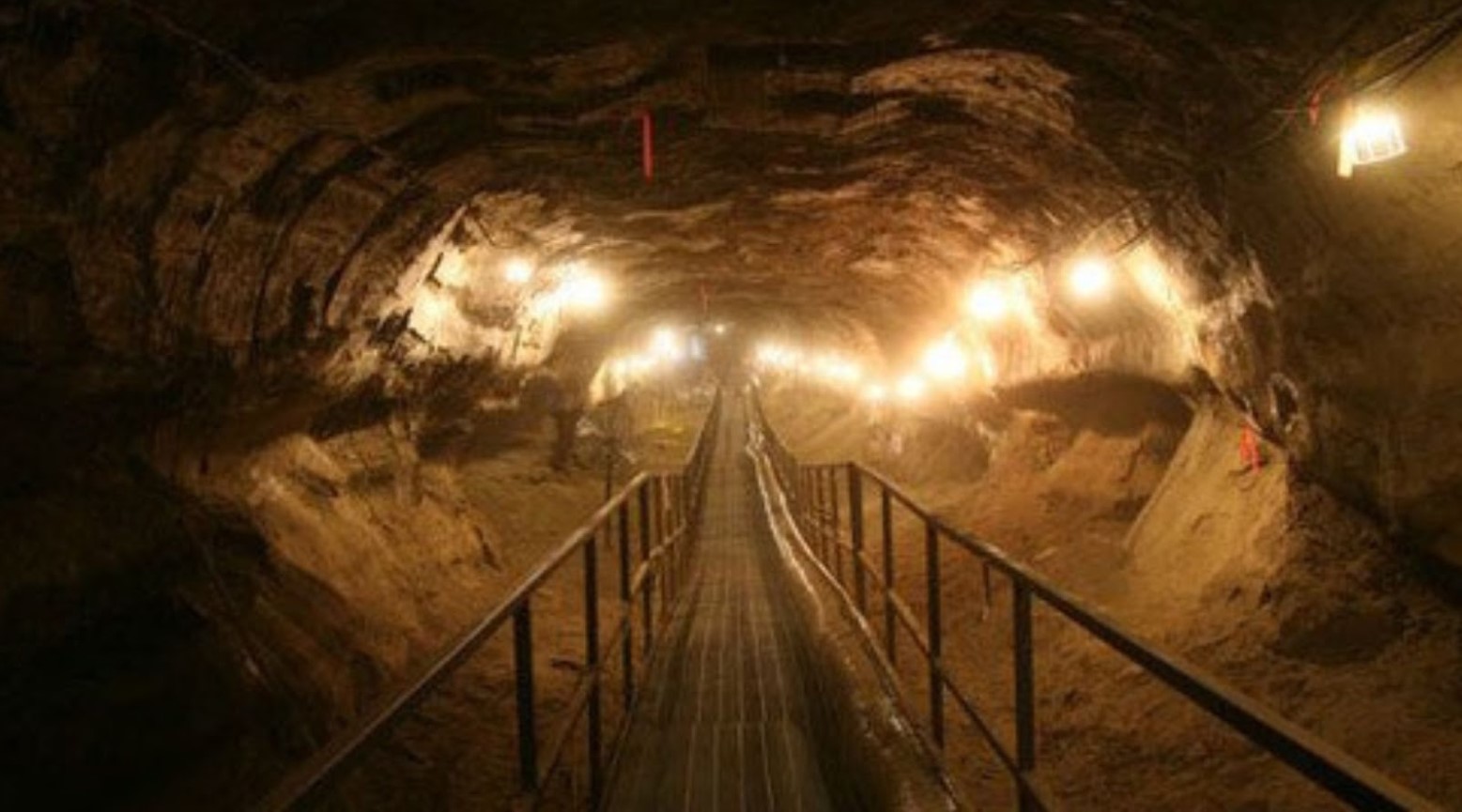 A permafrost tunnel in Alaska. Lights along the sides of it light up the tunnel, and a path with rails on either side goes through the tunnel.