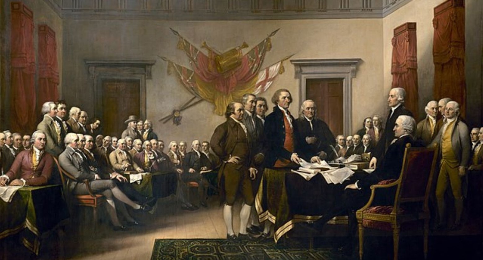 A painting of the Declaration of Independence. One man is sitting behind a desk. Some men are standing around him, and others are sitting before them.