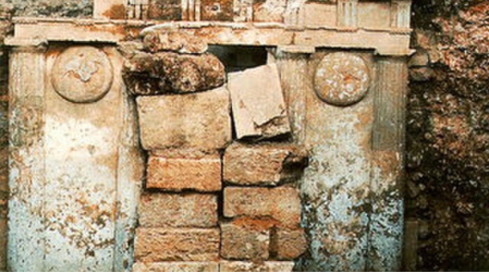 This is an ancient Macedonian tomb found in Greece. It has pillars and large stones blocking the entrance.