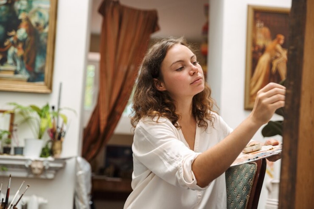 A woman is pictured looking at a piece of art hanging on a wall