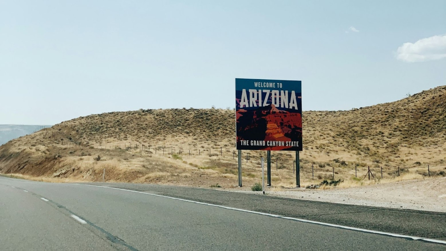 An Arizona welcome sign on the side of a road, seen in the daytime.