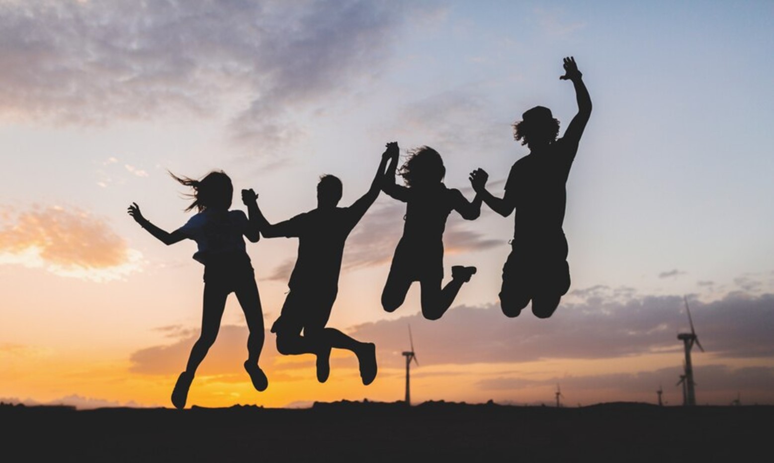 Four young people silhouetted as they jump in front of a setting sun