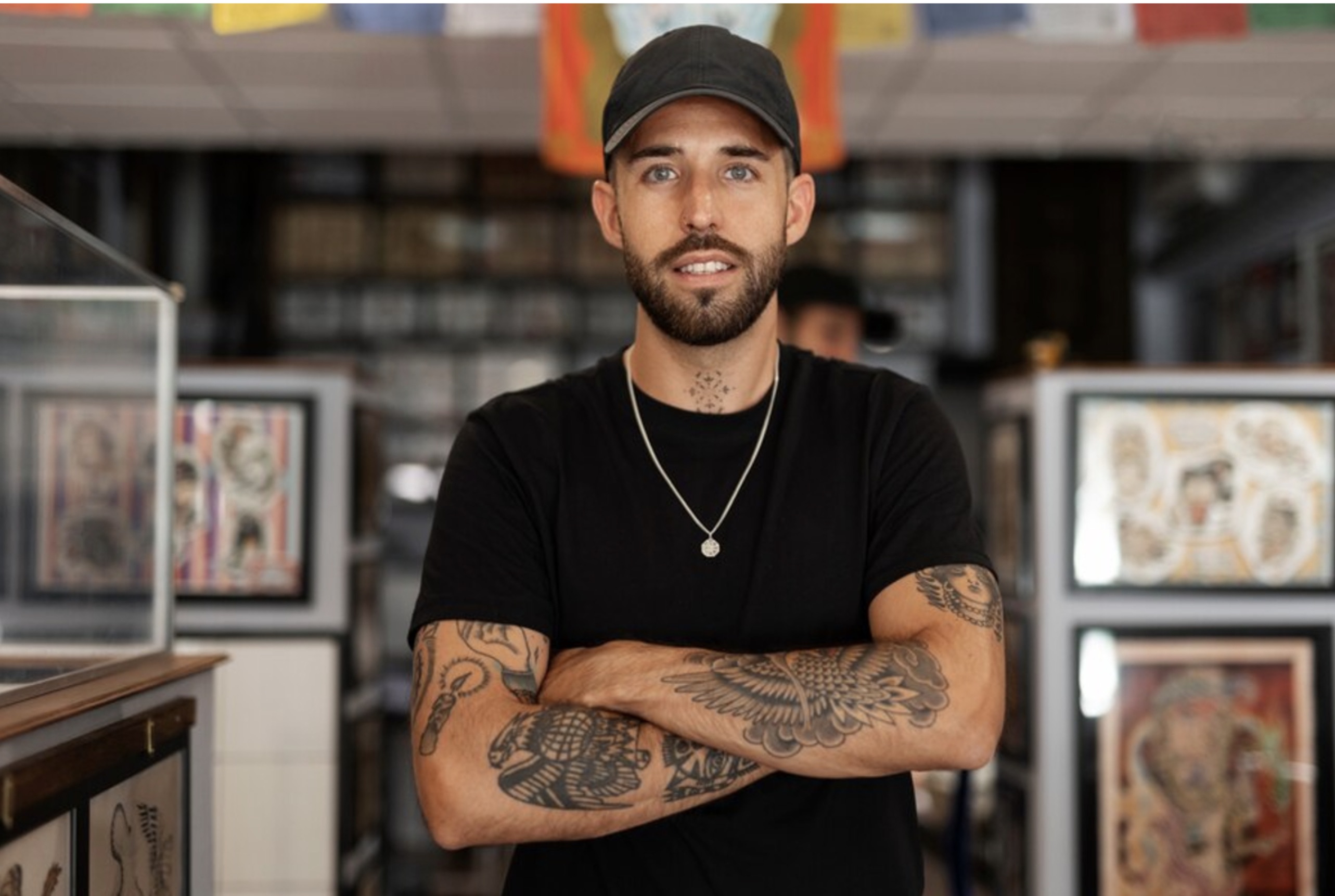 A man with several large tattoos on his arms stands in a tattoo studio