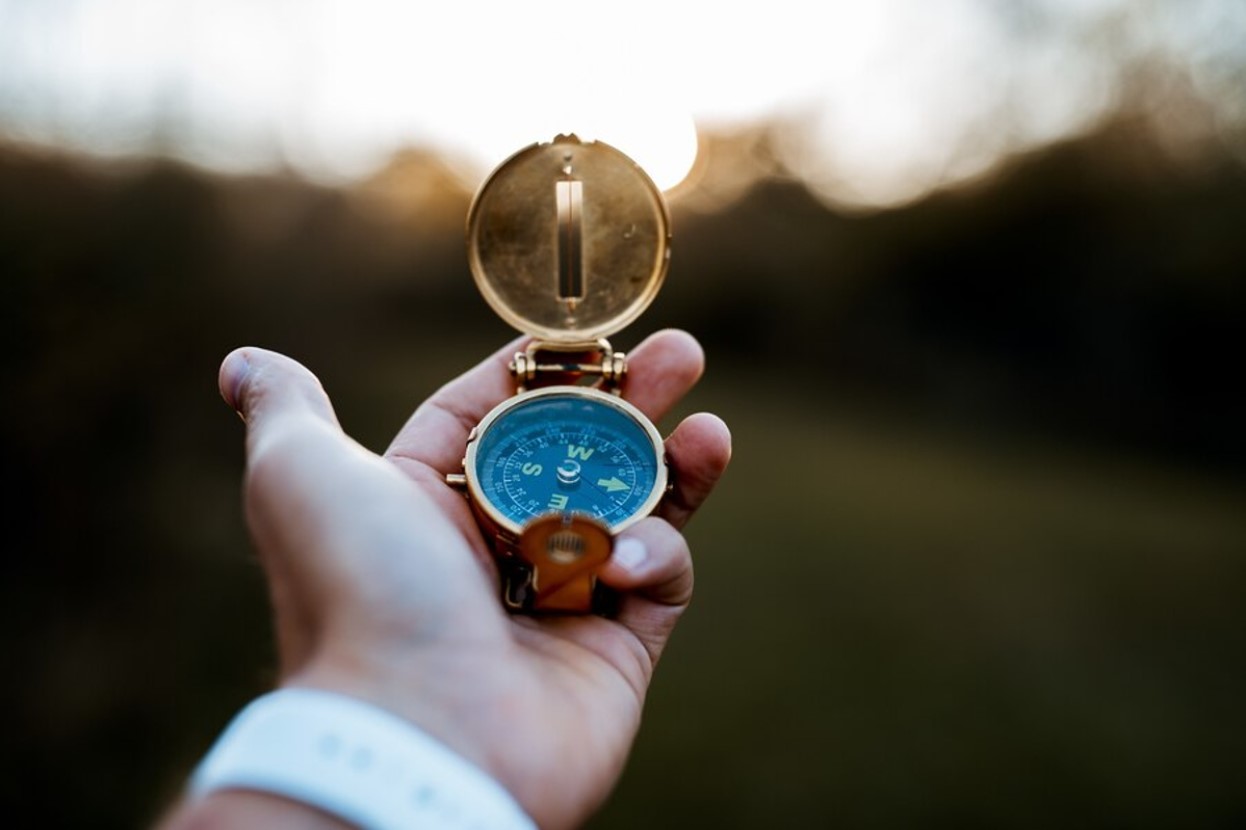 A hand reaching out while holding a small blue and gold compass