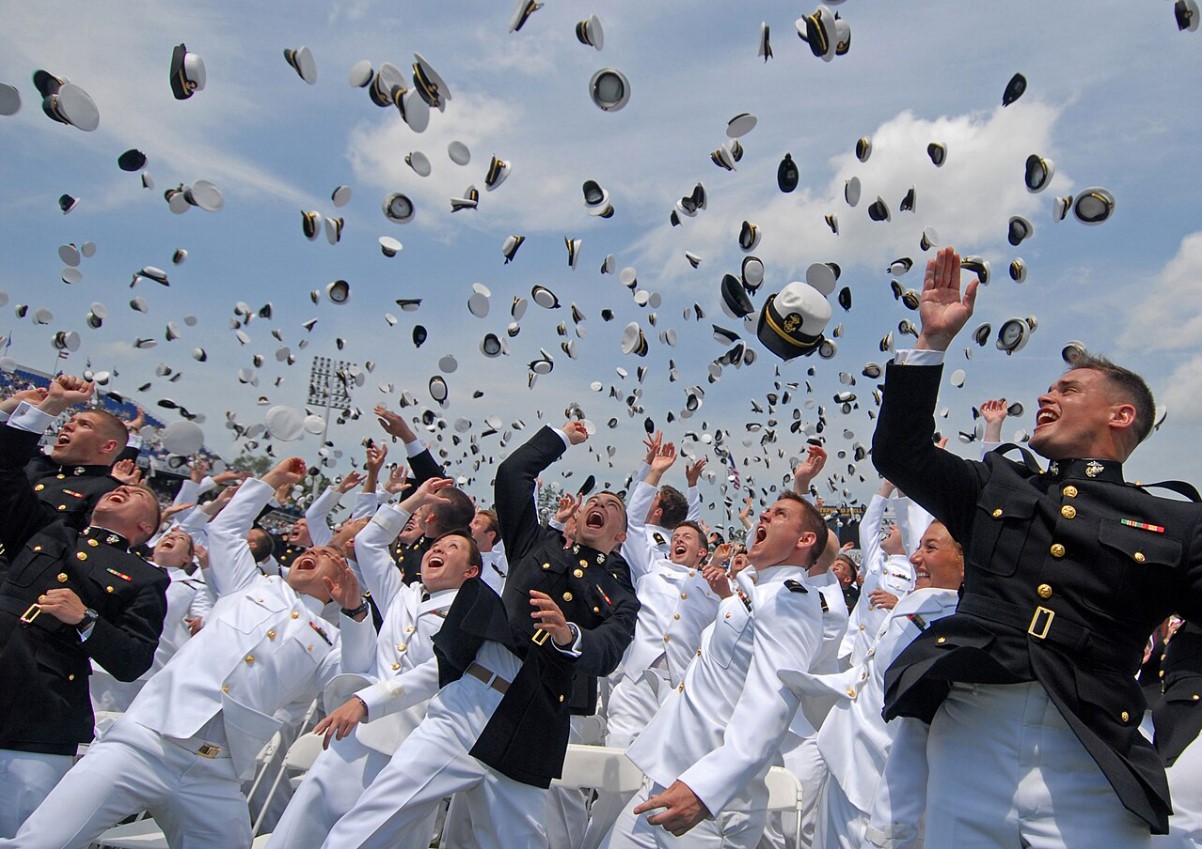 An image of several US Navy graduates throwing their hats into the air