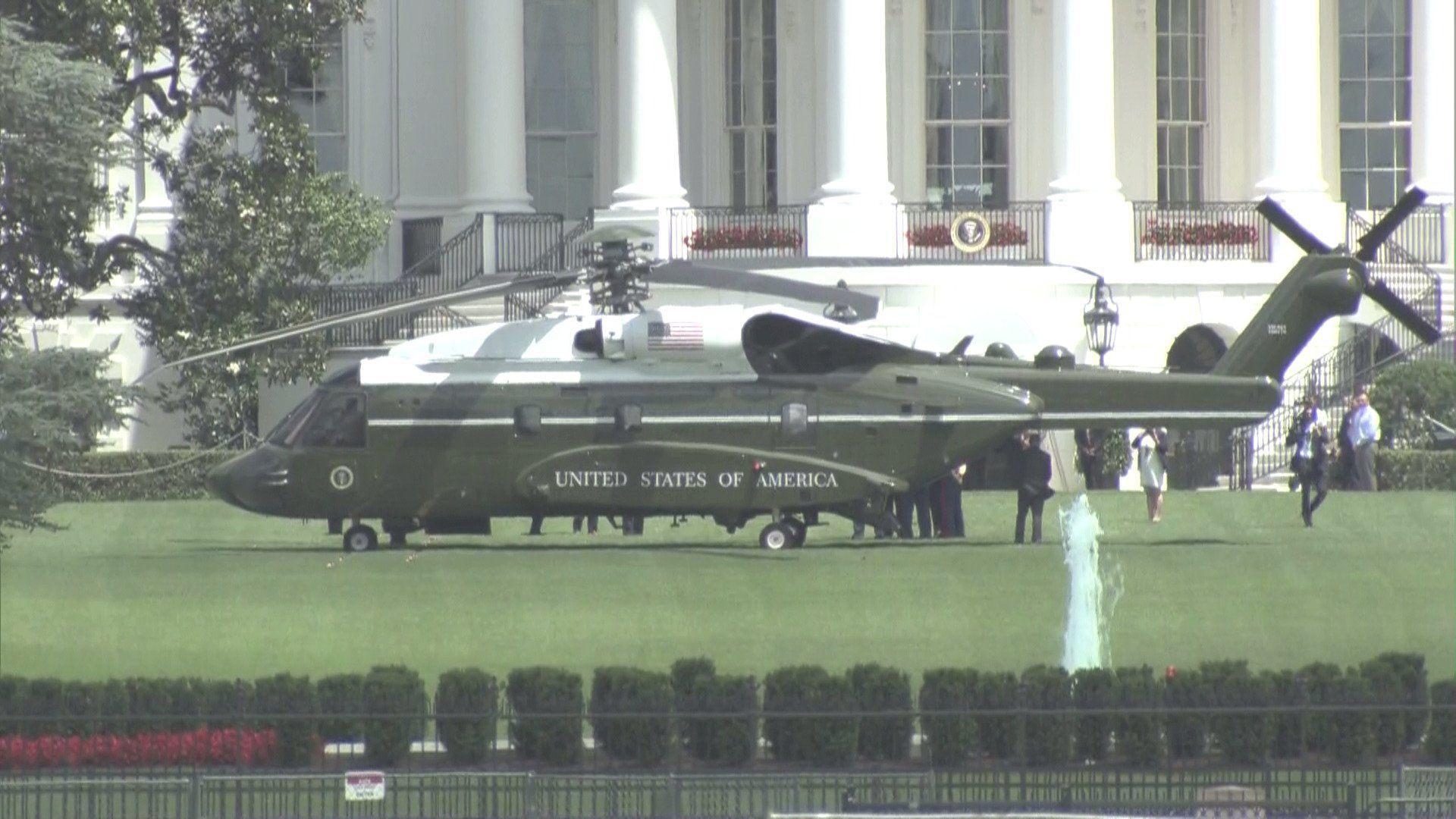 The VH-92 helicopter landed on the lawn before the White House. People in suits are walking around it.