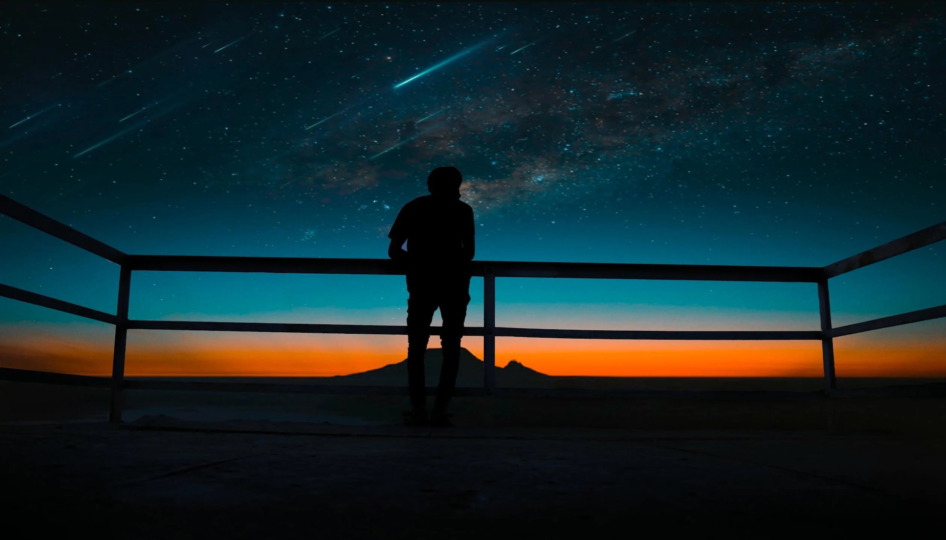 A silhouette of a person watching a shooting star in the evening sky