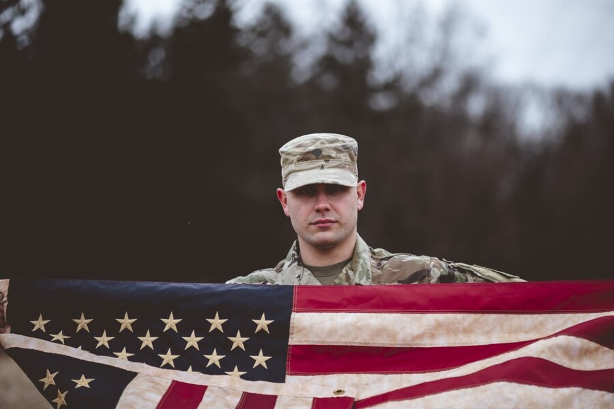 A US soldier in uniform holds up an American flag